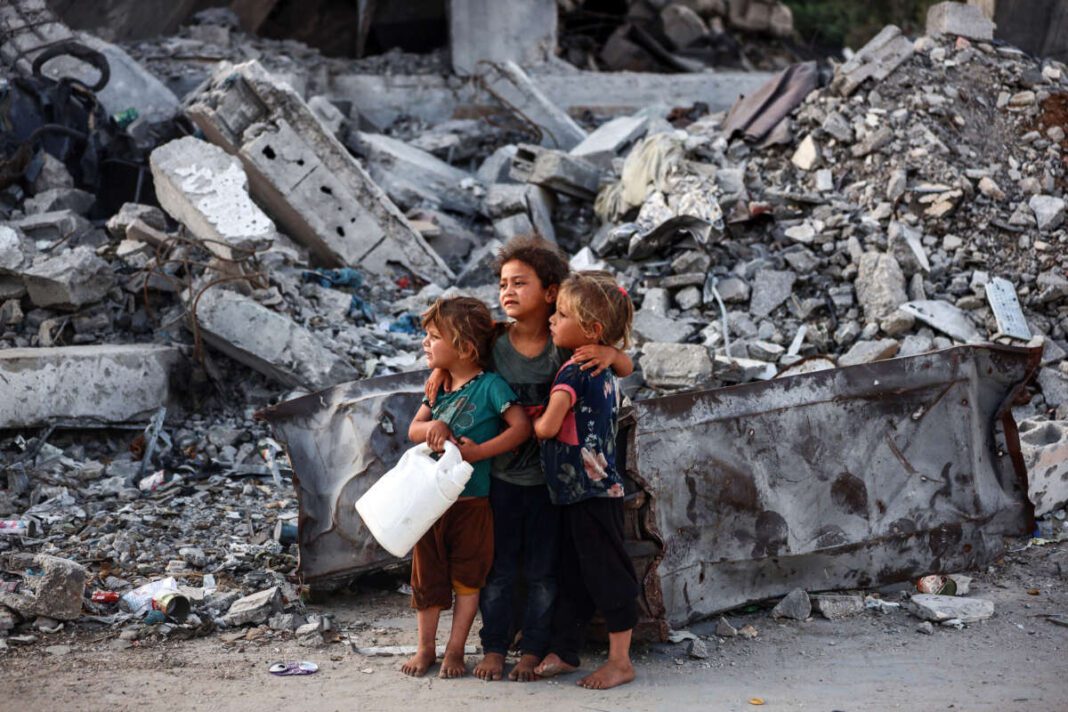 Três crianças palestinas abraçadas entre os escombros em Gaza